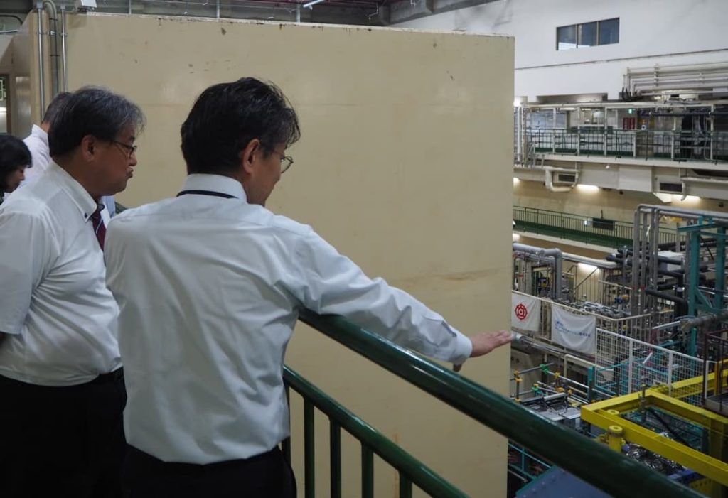 筑波実験棟にてBelleⅡ測定器を見ながら研究者から説明を受ける淵上研究振興局長（左）